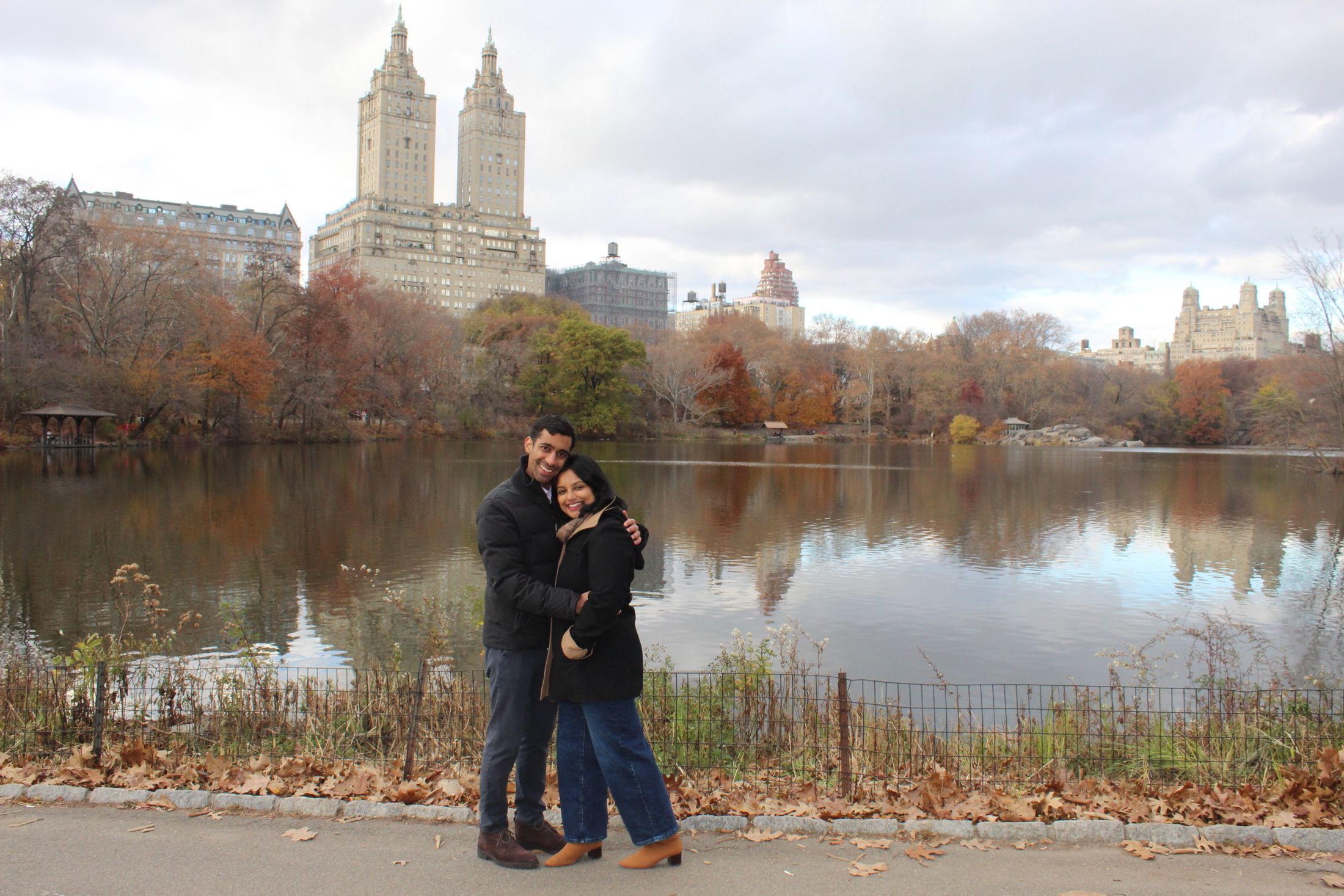 Manu and Nikhil by the lake in Central Park, the Upper West Side skyline behind them